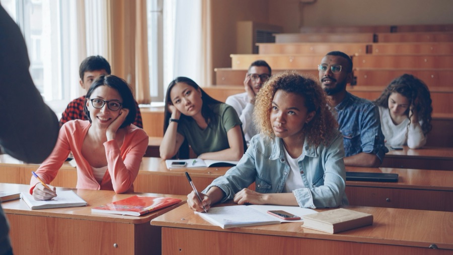 Students taking notes at their desks in a bright lecture hall